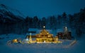 Traditional bright lit log cabin situated atop a snow covered mountain captured at night Royalty Free Stock Photo