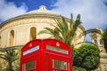 Mosta, Malta - Traditional British red telephone box with palm trees and the famous Mosta Dome at background