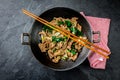 Traditional chinese mongolian beef stir fry in chinese cast iron wok with cooking chopsticks, stone slate background Royalty Free Stock Photo