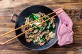 Traditional chinese mongolian beef stir fry in chinese cast iron wok with cooking chopsticks, wooden background. Top Royalty Free Stock Photo