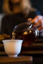 Traditional Chinese Tea Ceremony. Black or Red Tea pouring By a Blonde Caicasian girl into White pial cup on dark Table Royalty Free Stock Photo