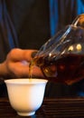 Traditional Chinese Tea Ceremony. Black or Red Tea pouring into White pial cup on dark Table background Royalty Free Stock Photo