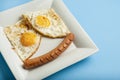 Traditional Clasic Breakfast Fried Eggs and Sausage on a white Square Porcelain Plate. Isoalted on Blue Background.