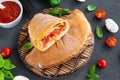 Traditional closed Italian calzone pizza with tomato sauce, mozzarella cheese and mushrooms on a board on a dark background.