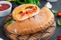 Traditional closed Italian calzone pizza with tomato sauce, mozzarella cheese and mushrooms on a board on a dark background.