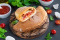 Traditional closed Italian calzone pizza with tomato sauce, mozzarella cheese and mushrooms on a board on a dark background.