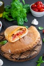 Traditional closed Italian calzone pizza with tomato sauce, mozzarella cheese and mushrooms on a board on a dark background.