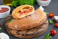 Traditional closed Italian calzone pizza with tomato sauce, mozzarella cheese and mushrooms on a board on a dark background.