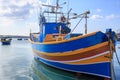 Traditional fishing boat, luzzu, anchored at Marsaxlokk, Malta. Blue sky with clouds and village background. Close up view. Royalty Free Stock Photo