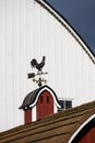 Traditional coper rooster weathervane on a classic red barn cupola, larger white barn in background Royalty Free Stock Photo