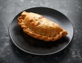 Traditional Cornish pasty filled with beef meat, potato and vegetables on black plate