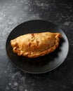 Traditional Cornish pasty filled with beef meat, potato and vegetables on black plate