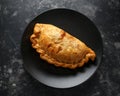 Traditional Cornish pasty filled with beef meat, potato and vegetables on black plate