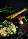 Traditional delicious pasta with chicken, mushrooms, broccoli, cream sauce and green olives on black plate and uncooked spagetti