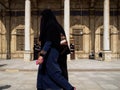 A traditional dressed and veiled egyptian woman passing by a mosque