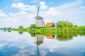 Traditional Dutch windmill and building with orange roof together among long grass reflected in mirror imaged in calm water Royalty Free Stock Photo