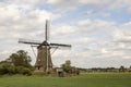 Traditional dutch windmill in the countryside in the Netherlands surrounded by pasture under a cloudy sky.