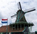 Traditional Dutch windmill under an overcast sky with the flag of the Netherlands flying in a strong wind Royalty Free Stock Photo