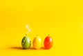 Traditional Easter decor. Group of bright paraffin extinguished candle with smoke in the shape of colorful eggs on warm yellow Royalty Free Stock Photo