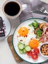 Traditional Englis breakfast plate with bacon strips, sunny side up eggs, vegetables and cake on light background Royalty Free Stock Photo