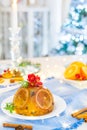 Traditional English Christmas pudding decorated with oranges and flowers in festive table setting with fruits, spices, lights of Royalty Free Stock Photo