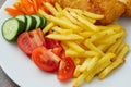 Traditional english dish with battered white cod, french fries and fresh vegetable served on a white plate. Close up