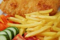 Traditional english dish with battered white cod, french fries and fresh vegetable served on a white plate. Close up