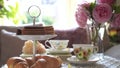 Traditional English tea time, Afternoon tea ceremony with cuppa tea, croissants, crackers and biscuits on hight tea stand in pink 