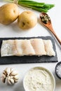 Traditional fish and chips ingredients recipe  raw cod fillets on stone slate  batter, potatoe, tartar sauce, lemon, capers , Royalty Free Stock Photo