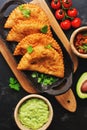 Traditional fried empanadas served with tomato and avocado sauce on a dark background. Top view, copy space