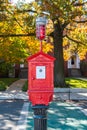 Traditional Game Well Boston fire alarm station box on a pedestal in front of beautiful fall trees on a sunny fall day