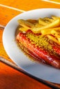 Traditional German currywurst, served with chips on a white plate. Wooden table as background