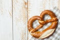 Traditional German savory lye pretzel with salt on checkered cotton kitchen towel on white plank wood table. Poster banner