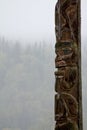 Traditional Gitxsan totem pole with mist covered forest behind