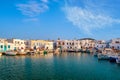 Traditional Greek fishing village and harbour on sunny day, boats moored by jetty and whitewashed houses alongside.