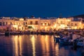 Traditional Greek fishing village and harbour after sunset, boats moored by jetty, street lamps and whitewashed houses