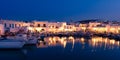 Traditional Greek fishing village and harbour after sunset, boats moored by jetty, street lamps whitewashed houses