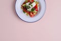 Traditional Greek salad with feta cheese and vegetables served in white plate over bright pastel pink background. Royalty Free Stock Photo