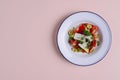 Traditional Greek salad with feta cheese and vegetables served in white plate over bright pastel pink background. Royalty Free Stock Photo