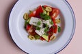 Traditional Greek salad with feta cheese and vegetables served in white plate over bright pastel pink background. Royalty Free Stock Photo