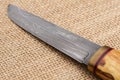 Traditional handmade Finnish knife with the abstract wave pattern of damascus steel and wooden handle over an old sack background. Royalty Free Stock Photo