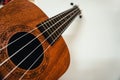 Close up of brown Ukulele on white background. Ukulele strings, saddle, soundhole, ukulele body, neck, fretboard.