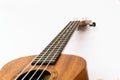 Close up of brown Ukulele on white background. Ukulele strings, saddle, soundhole, ukulele body, neck, fretboard.