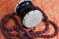 Traditional hindu prayer beads rudraksha and musical instrument of God Shiva Damaru drum on a red saree background