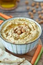 Traditional hummus made with chickpeas, olive oil, and garlic in a bowl with vegetable sticks and pita bread on wood