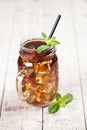 Traditional iced tea with lemon, mint leaves and ice cubes in glass jar on rustic wooden table