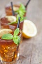 Traditional iced tea with lemon, mint leaves and ice cubes in glasses on rustic wooden table background