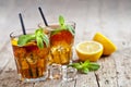 Traditional iced tea with lemon, mint leaves and ice cubes in glasses on rustic wooden table