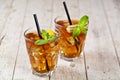 Traditional iced tea with lemon, mint leaves and ice cubes in two glasses on rustic wooden table