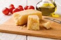 Traditional iitalian hard cheese Grana Padano or Parmesan on a brown cuting board near small red tomatoes and olive oil over white